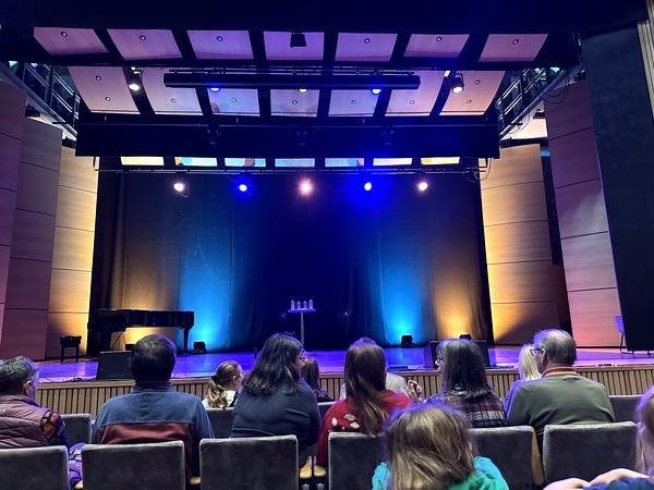 An audience facing a stage lit in blue