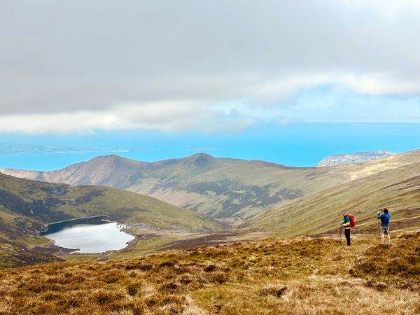 Walkers crossing open hills above a mountain lake
